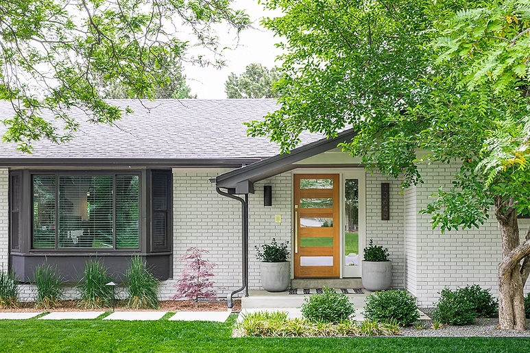 White brick ranch home with a wood front door framed by mature trees